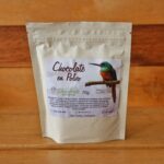 Envase de chocolate en polvo 100% natural de 70g con clavos y canela, colocado sobre una superficie rústica