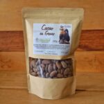 Bolsa de semillas de cacao tostadas de 250g, colocada sobre una superficie rústica con granos de cacao alrededor.