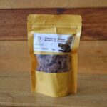 Pequeño paquete de semillas de cacao con panela y chocolate de 50g, acompañado de granos de cacao y trozos de chocolate artesanal sobre una superficie rústica.